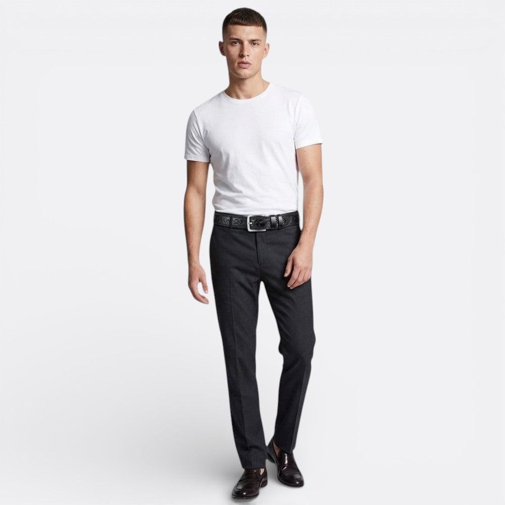 Le Monde de la Ceinture black leather tribal embossed belt with silver buckle, styled with a white t-shirt and grey trousers.